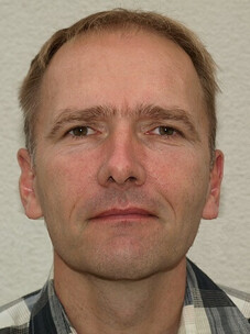 Herr Klauss mit neutralem Gesichtsausdruck und kurzem Haar, Stirnrunzeln.